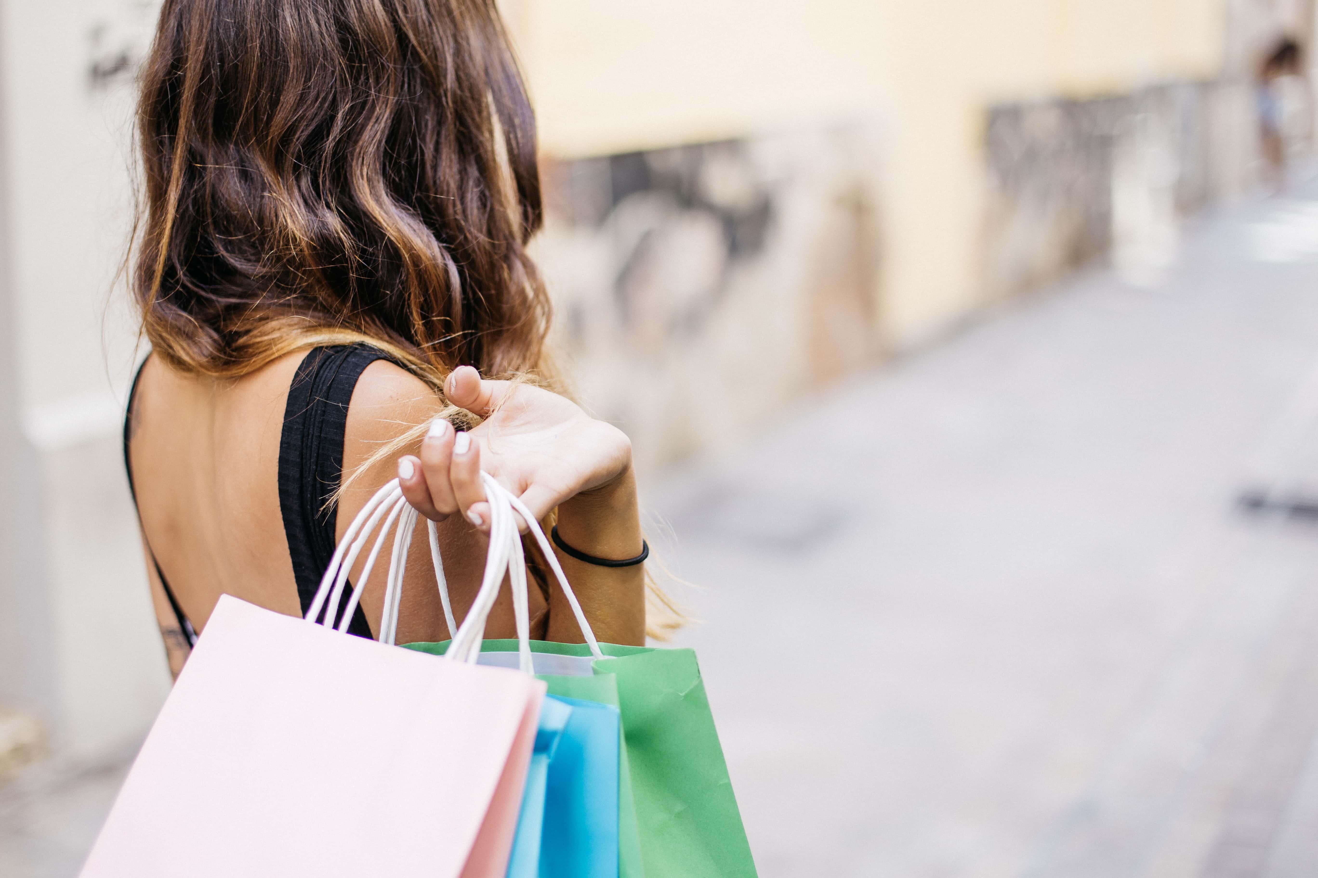 Mulher de costas, segurando várias sacolas de compras